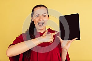 Portrait of young Caucasian woman posing with tablet isolated on yellow background.