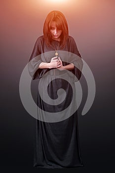 Portrait of a young caucasian woman praying. Prayer girl dressed in Vestments of a nun on gray studio background