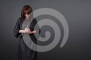 Portrait of a young caucasian woman praying. Prayer girl dressed in Vestments of a nun on gray studio background