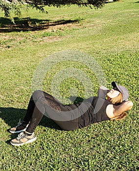 Portrait of a young Caucasian woman in sportswear stretched out on the grass in a park doing sit-ups. Concept of outdoor pursuit