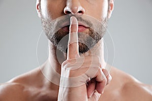 Portrait of a young charming naked man showing silence gesture