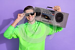 Portrait of young cheerful attractive cool student guy smiling touch specs hold boombox listen loud music disco isolated