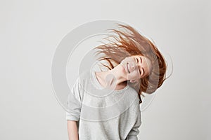 Portrait of young cheerful beautiful redhead girl smiling with closed eyes shaking head and hair over white background.