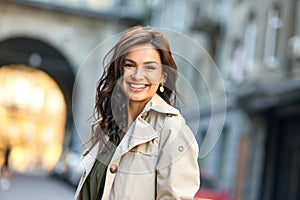 Portrait of a young cheerful caucasian woman looking at camera and smiling while standing on the city street