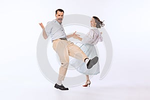 Portrait of young cheerful couple, man and woman in retro outfit dancing isolated over white studio background. Emotive