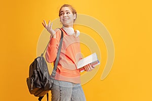 Portrait of young cheerful girl, student in casual cloth and backpack posing isolated over yellow studio background