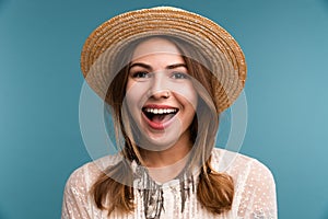 Portrait of a young cheerful girl in summer hat isolated over blue background,