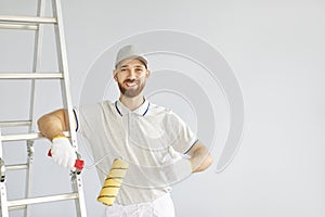 Portrait of young cheerful happy professional painter with paint roller in hands looking at camera