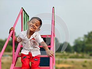 Portrait of a young cheerful Indian boy standing on the chairs of a playground