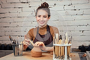 Portrait of a young and cheerful woman holding a vase of clay. The potter works in a pottery workshop with clay. the