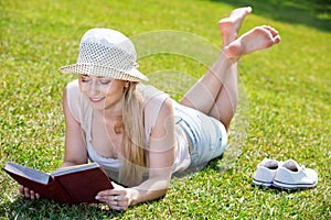 Portrait of l woman lying on green lawn in park and reading book