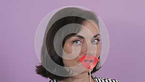 Portrait of a young cheerful woman putting on a carnival paper mask of red lips slow motion