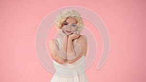 Portrait of young cheerful woman in wig, white dress and with red lipstick on lips in studio on pink background. Woman