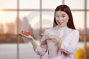 Portrait of young chineese businesswoman holding gift box and pointing at it.