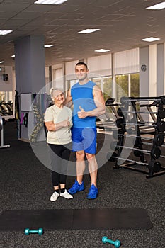 Portrait of a young coach in uniform and an old woman in gym. Physical culture for older people. Training and individual