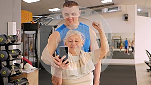 Portrait of a young coach in uniform and an old woman in gym. Physical culture for older people. Training and individual