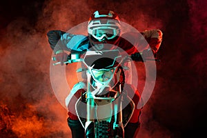 Portrait of young concentrated man, biker developing speed on motorbike isolated over dark background in neon light with