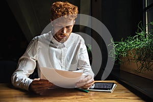 Portrait of young concentrated readhead bearded man, sitting at