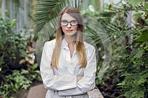 Portrait of young confident Caucasian woman, scientist, botanist, agronomist, wearing glasses and white lab coat, posing