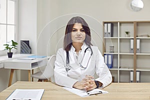 Portrait of young confident female doctor or nurse sitting at desk at her workplace.