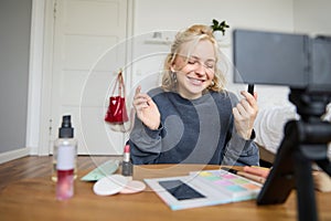 Portrait of young content maker, woman blogger recording a video on digital camera, showing lipstick colour to her