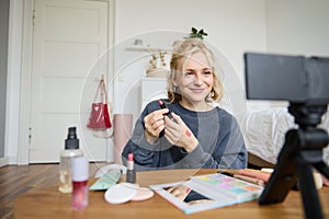 Portrait of young content maker, woman blogger recording a video on digital camera, showing lipstick colour to her