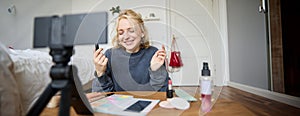 Portrait of young content maker, woman blogger recording a video on digital camera, showing lipstick colour to her