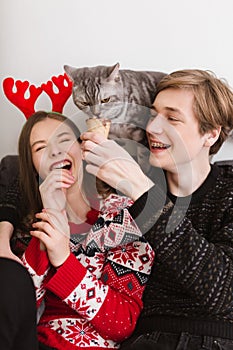 Portrait of young cool couple sitting on sofa at home with ice-cream in hands and happily spending time together while