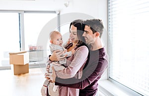 A portrait of young couple with a baby and cardboard boxes moving in a new home.