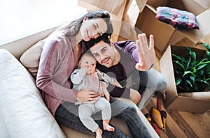 A portrait of young couple with a baby and cardboard boxes moving in a new home.