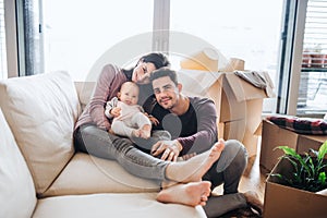 A portrait of young couple with a baby and cardboard boxes moving in a new home.