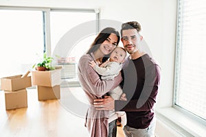 A portrait of young couple with a baby and cardboard boxes moving in a new home.