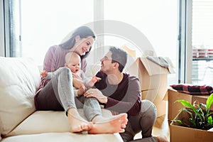 A portrait of young couple with a baby and cardboard boxes moving in a new home.