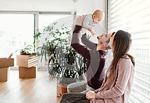 A portrait of young couple with a baby and cardboard boxes moving in a new home.