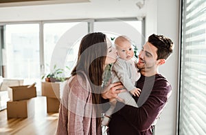 A portrait of young couple with a baby and cardboard boxes moving in a new home.