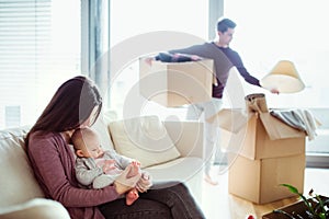 A portrait of young couple with a baby and cardboard boxes moving in a new home.