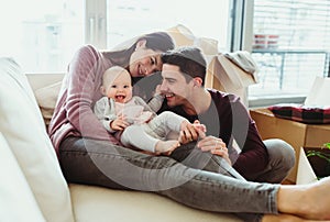 A portrait of young couple with a baby and cardboard boxes moving in a new home.