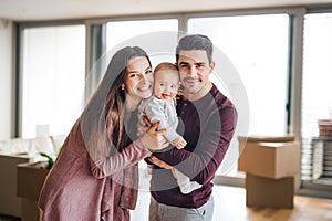 A portrait of young couple with a baby and cardboard boxes moving in a new home.