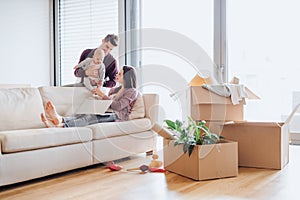 A portrait of young couple with a baby and cardboard boxes moving in a new home.