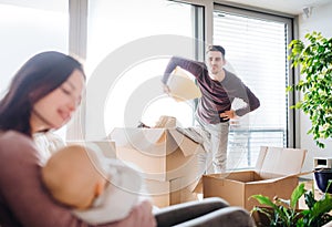 A portrait of young couple with a baby and cardboard boxes moving in a new home.