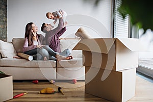 A portrait of young couple with a baby and cardboard boxes moving in a new home.