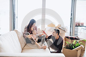 A portrait of young couple with a baby and cardboard boxes moving in a new home.