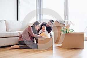 A portrait of young couple with a baby and cardboard boxes moving in a new home.