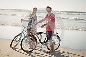 Portrait of young couple with bicycles standing at beach