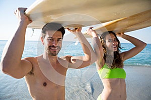 Portrait of young couple carrying surfboard at beach