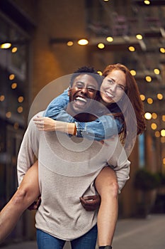 Portrait Of Young Couple Enjoying City Life Heading For Night Out With Man Giving Woman Piggyback