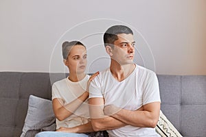 Portrait of young couple having conflict, offended man sitting on sofa and turning away from wife, having family fight or quarrel