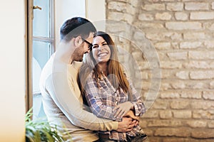 Young couple hugging next to the window, brick wall background