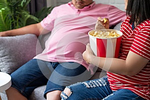 Portrait of young couple laughing, eating popcorn, sitting on the sofa watching TV at home