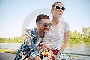 Portrait of young couple, laughing woman and her boyfriend going for a bike ride on a sunny summer day. Romantic